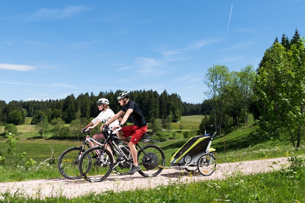 Schoenwald_E-Bike-Touren_im_Schwarzwald Familie fährt auf E-Mountainbikes mit Anhänger durch Schwarzwaldlandschaft
